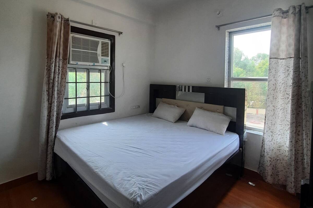 A bedroom with a bed, a ceiling fan, a window with curtains, and an air conditioning unit.