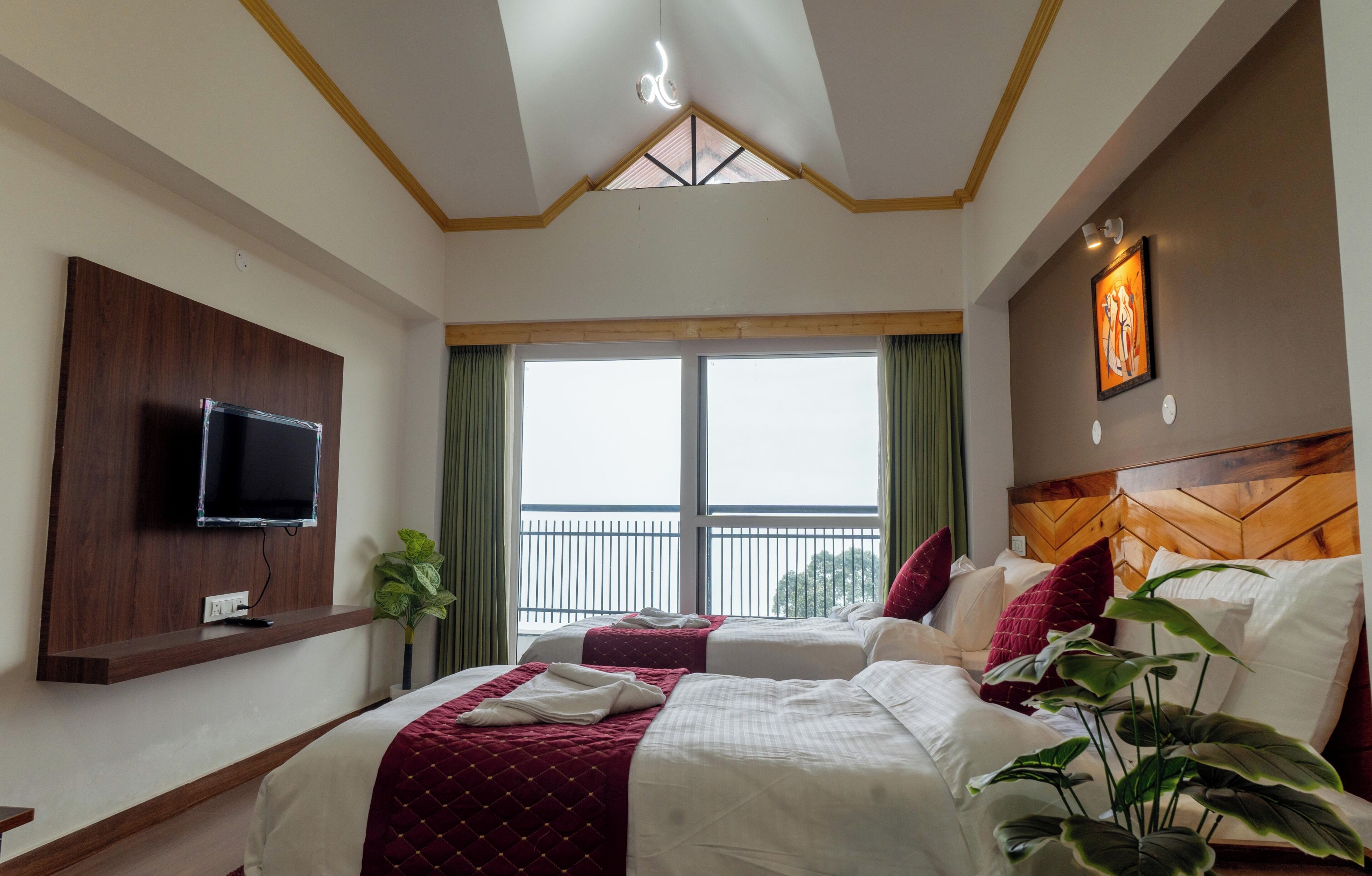 Habitación de hotel con dos camas, televisor montado en la pared, vista al balcón y lámpara en el techo.