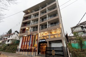 Un hôtel à plusieurs étages, doté de balcons, d’une entrée sécurisée et de drapeaux.