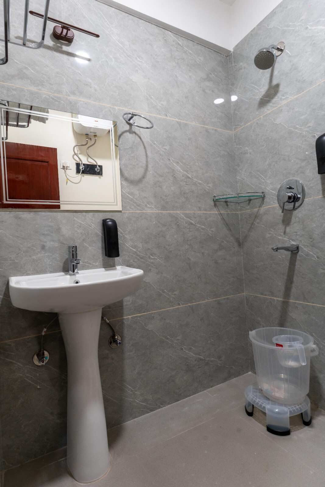 Un bany amb un lavabo amb pedestal, un mirall, una dutxa i un petit safataixa.