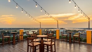 Eine Dachterrasse mit Tischen, Stühlen, Lichterketten und Blick auf Stadt und Fluss.