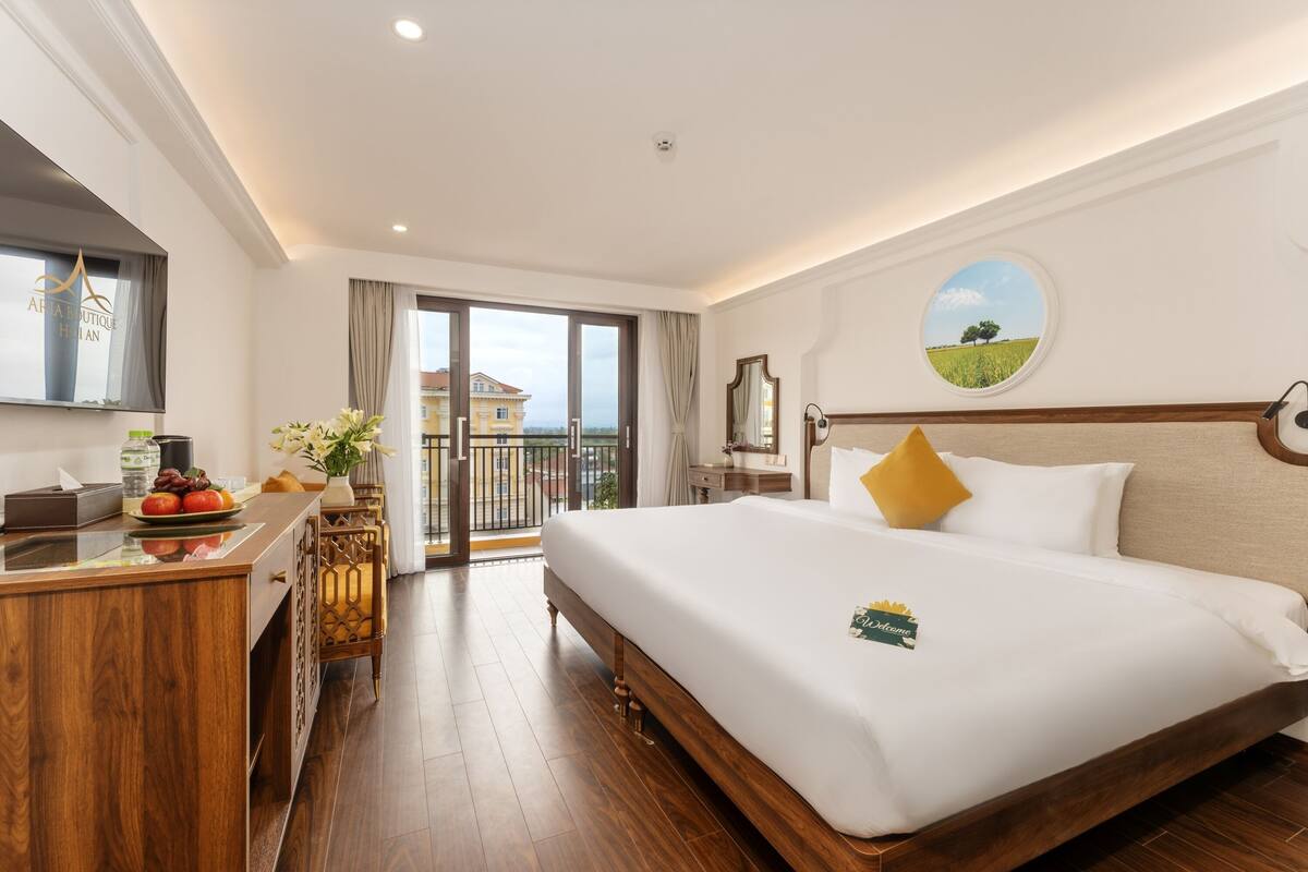 Een hotelkamer met een bed, een bureau met een bloevas, uitzicht naar buiten en een rond schilderij aan de muur.