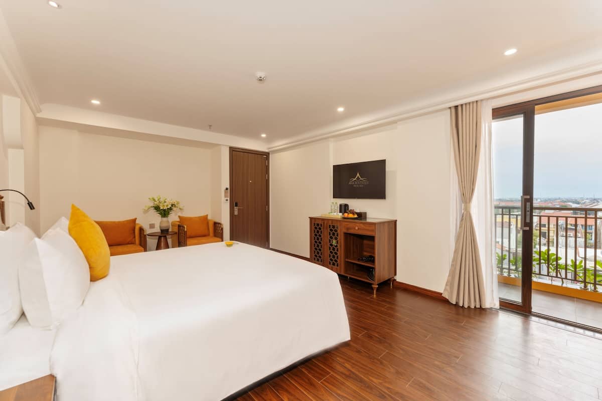 Een hotelkamer met een groot bed, een bureau, een televisie en een balkon met uitzicht op de stad.