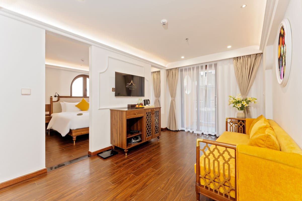 Een hotelkamer met een bed, een televisie, een houten kast, een gele bank en een groot raam met gordijnen.
