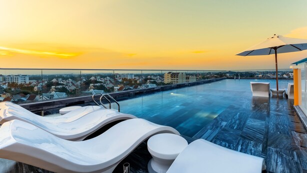 Ein Dachpool mit Liegestühlen und Blick auf die Stadt im Abendrot.
