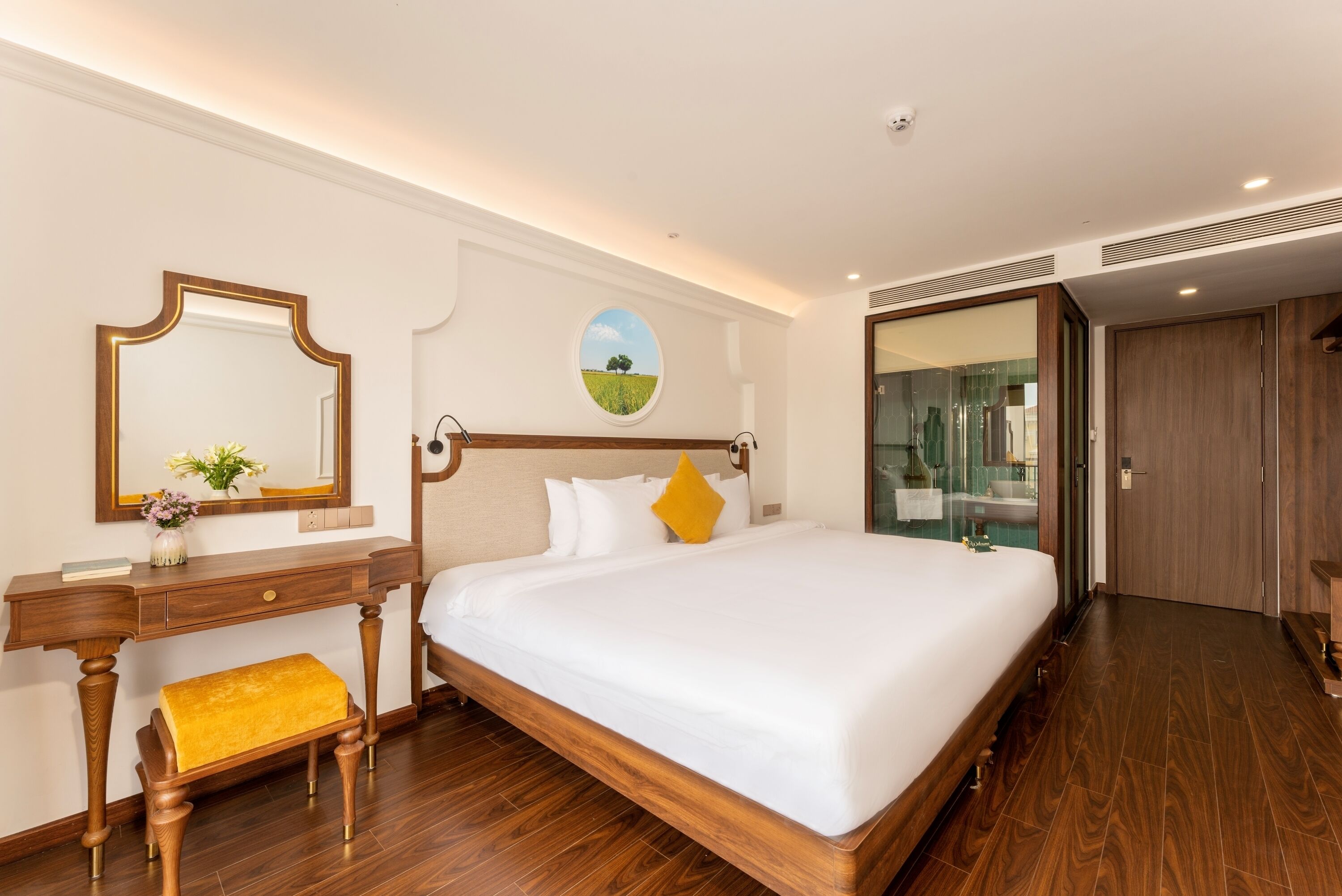 Una habitación de hotel con una cama grande, un escritorio de madera, un espejo y un adorno redondo en la pared.