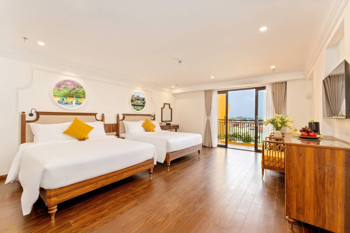 Een hotelkamer met twee bedden, een houten bureau, een balkon met uitzicht en een rond raam.