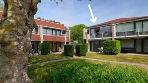 En boligbygning med rødt tag, store vinduer og en balkon.