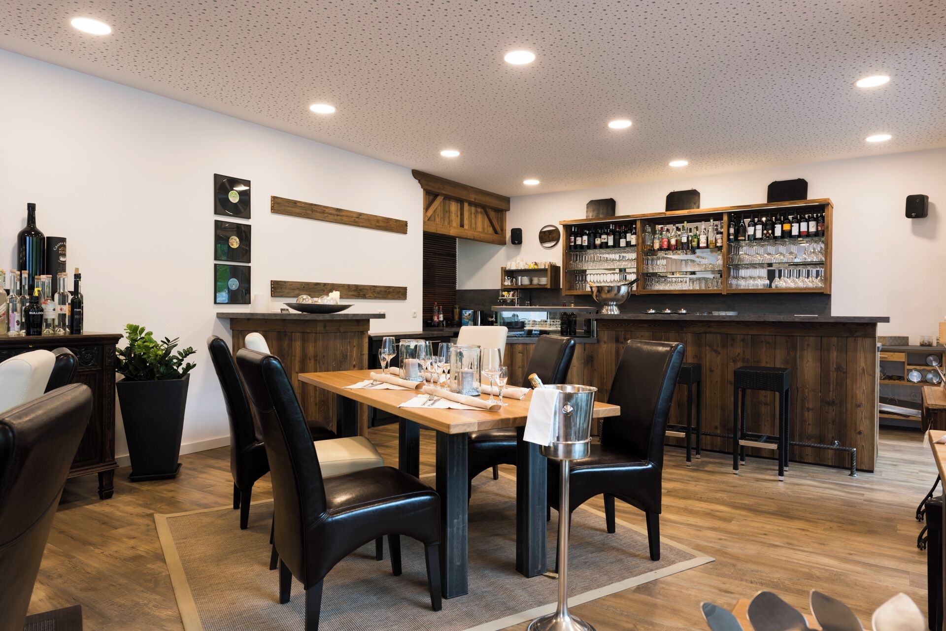 Un restaurant doté d’un bar en bois, de chaises en cuir noir et d’une table à manger dressée pour quatre personnes.