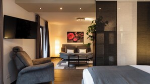 A modern hotel room with a bed, a sofa, a TV, and a large window.