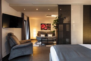 Ein modernes Hotelzimmer mit einem Bett, einer Couch, einem Fernseher und einem großen Fenster.