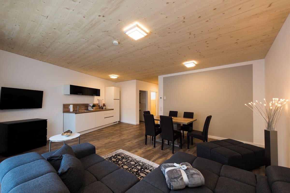 Una sala de estar moderna con un sofá, un televisor y un comedor con sillas y una mesa.
