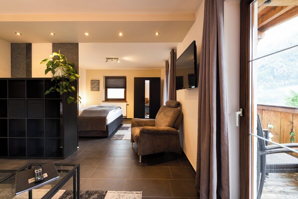 Una habitación moderna con cama, zona de estar, televisor y balcón con vistas.