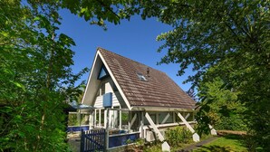 A house with a sloped roof, a fenced yard, and a swimming pool. - Holiday home Salvatorhoeve 120 nature house at Salvatorhoeve (Ouwerkerk)