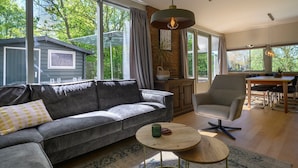 A modern living room with a grey sofa, a round wooden coffee table, and a dining area with a table and chairs. - Holiday home Salvatorhoeve 120 nature house at Salvatorhoeve (Ouwerkerk)
