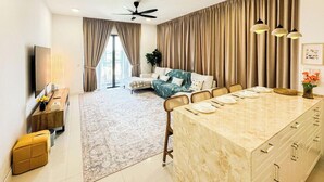 A modern living room with a sofa, a dining area with a marble island, and a large window with curtains. - The Legacy OUG by Airhost (Kuala Lumpur)