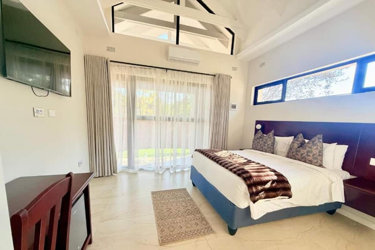A bedroom with a large bed, a TV, a desk, and a window with curtains.