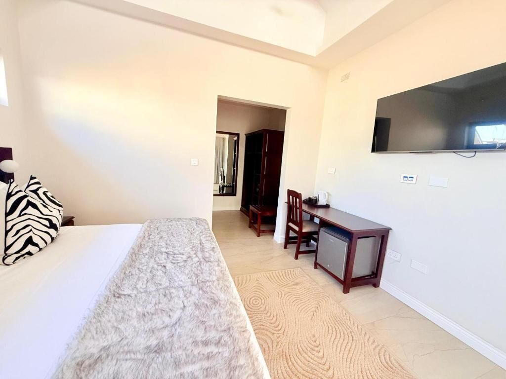 A bedroom with a bed, a desk, a chair, and a television on the wall.