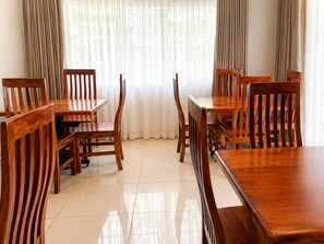 A dining area with wooden tables and chairs, a tiled floor, and a window with curtains. - 19 On Bay Noakes (Harare)
