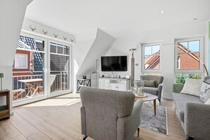 A modern living room with a flat-screen TV, grey sofas, and a dining area with a table and chairs. - Platzhirsch - New Platzhirsch vacation apartment in Greetsiel for relaxation (Krummhörn)