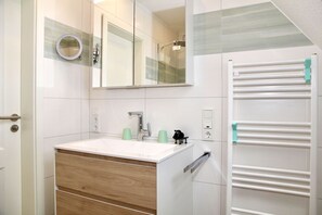 A bathroom with a white sink, mirror, and towel rack. - Platzhirsch - New Platzhirsch vacation apartment in Greetsiel for relaxed (Krummhörn)