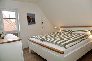 A bedroom with a bed, a desk, a window, and a picture on the wall. - Platzhirsch - New Platzhirsch vacation apartment in Greetsiel for relaxed (Krummhörn)