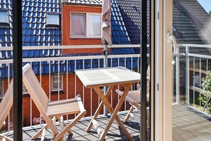Un balcón con mesa y sillas, vista a un edificio de ladrillo rojo con azulejos azules y una puerta de vidrio.