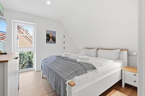Un dormitorio con cama, mesitas de noche, una ventana y una puerta.