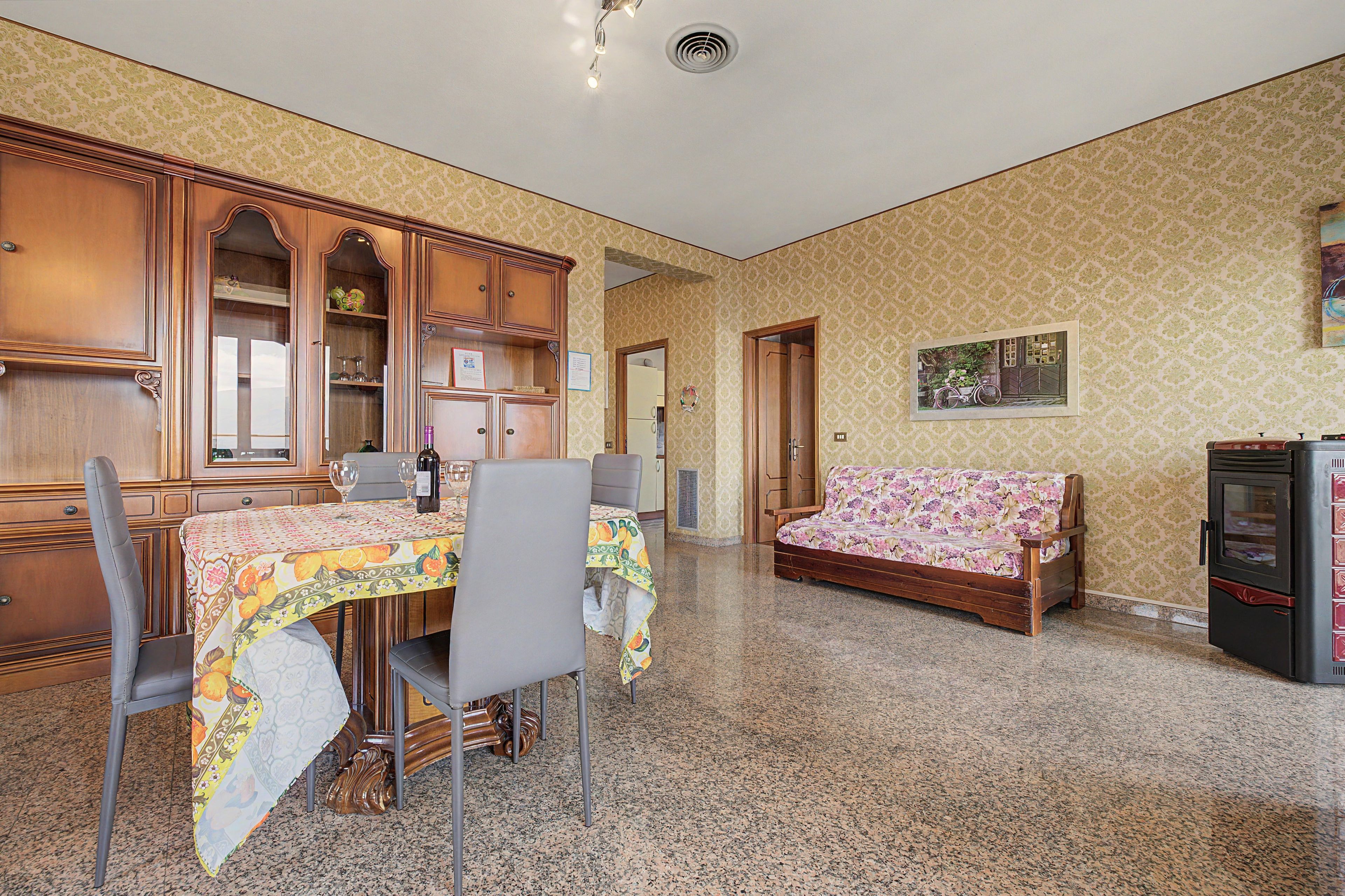 A dining area with a table set for two, a sofa, and a refrigerator.