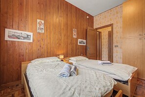 Une chambre d’hôtel aux murs lambrissés, avec deux lits recouverts de draps blancs, et une porte donnant sur une autre pièce.