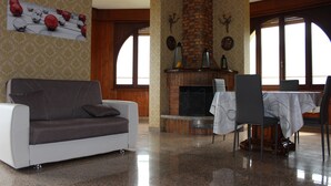 A living room with a sofa, a fireplace, and a dining area with chairs and a table. - Cozy 90 sqm apartment in Tignale with pool, garden, terrace, parking and Wi-Fi (Aer)