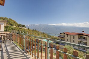 Ein Balkon mit Blick auf eine gebirgige Landschaft, ein Poolbereich und ein Gebäude mit rotem Dach.