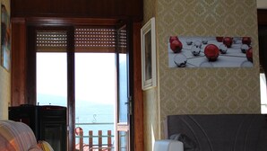 A living room with a sofa, a wooden table, and a view of the sea through a sliding door. - Cozy 90 sqm apartment in Tignale with pool, garden, terrace, parking and Wi-Fi (Aer)