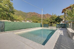 Une piscine rectangulaire à l’eau claire, entourée d’une terrasse en béton et d’une clôture verte.