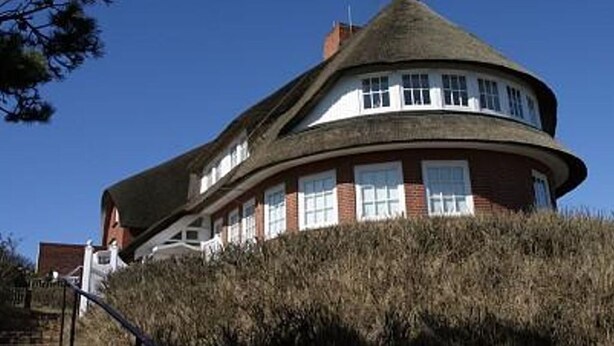 Una casa con techo curvo, paredes de ladrillo y varias ventanas.