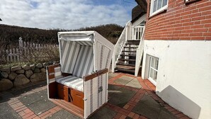 Un patio con una silla de mimbre, un sendero de ladrillo y una casa de fachada blanca con un muro de ladrillo rojo.