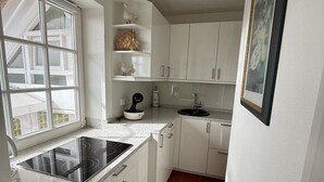 Una cocina con armarios blancos, una placa de inducción negra, una encimera blanca y una ventana.