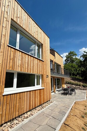 A modern wooden building with large windows, a balcony, and a patio area with outdoor seating. - Waterfall Soul (Triberg) - Terrace (Triberg im Schwarzwald)