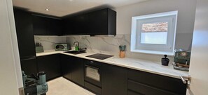 A modern kitchen with dark cabinetry, a built-in oven, a microwave, and a coffee machine. - Waterfall Soul (Triberg) - Terrace (Triberg im Schwarzwald)
