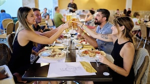 Eine Gruppe von Personen stöst in einem Restaurant am Tisch an, mit Speisekarte und Biergläsern.