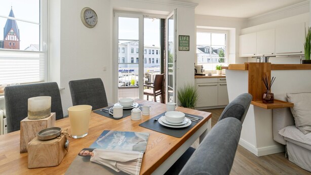 A modern kitchen with a dining area, a view of the city, and a clock on the wall. - Syltliebe - Modern and central app. for 4 persons with balcony, car (Sylt)