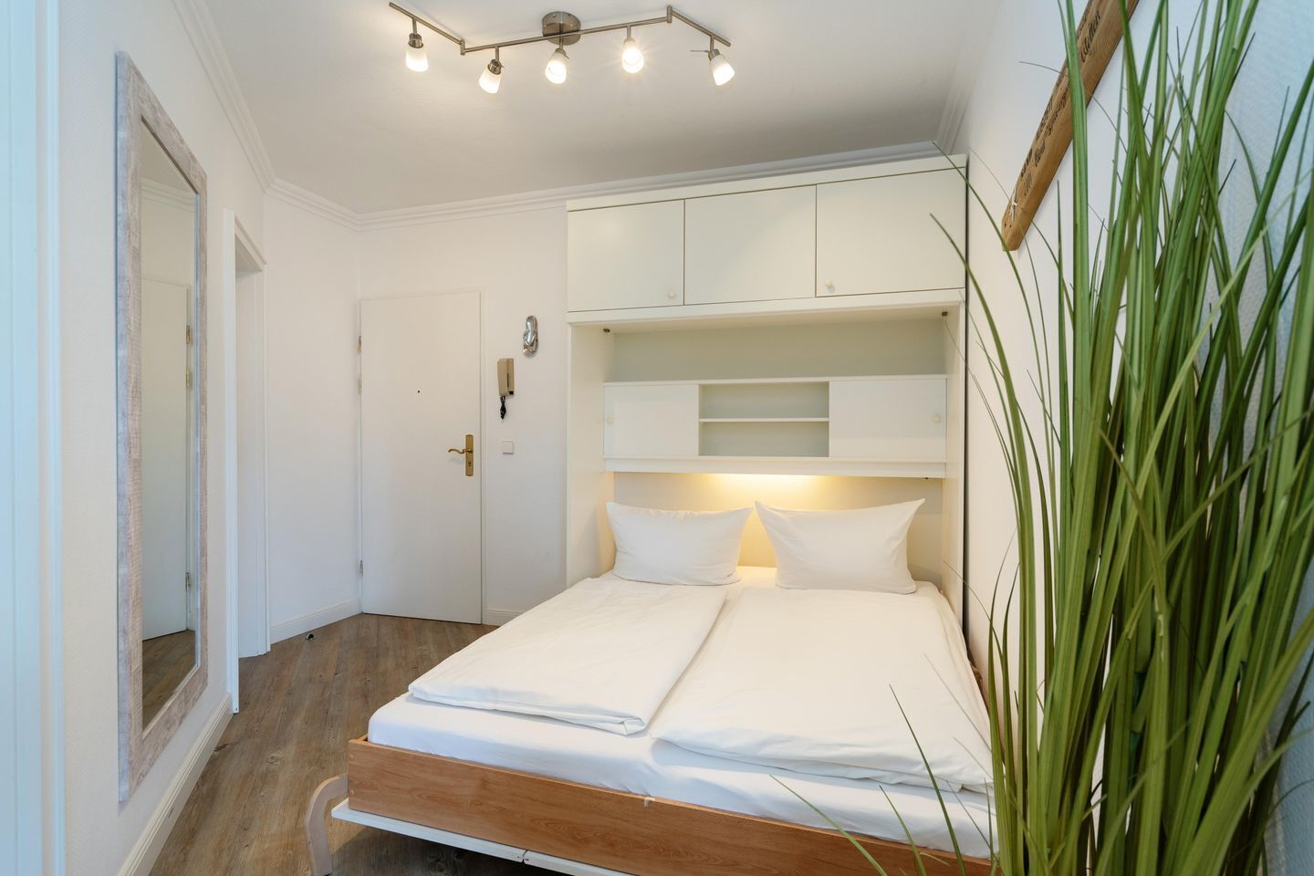 Un dormitorio con cama, mesitas de noche, una puerta y un espejo.