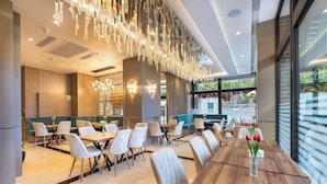 A modern dining area with wooden tables and chairs, a chandelier, and a view of the outdoors. - Davo Hotel (Târgu Neamț)