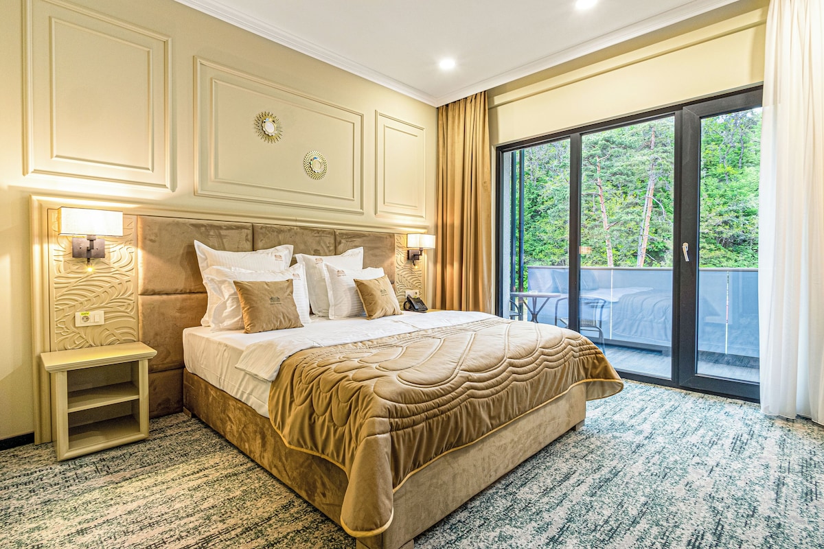 A hotel room with a large bed, bedside lamps, a nightstand, and a view of the outdoors through a sliding glass door.