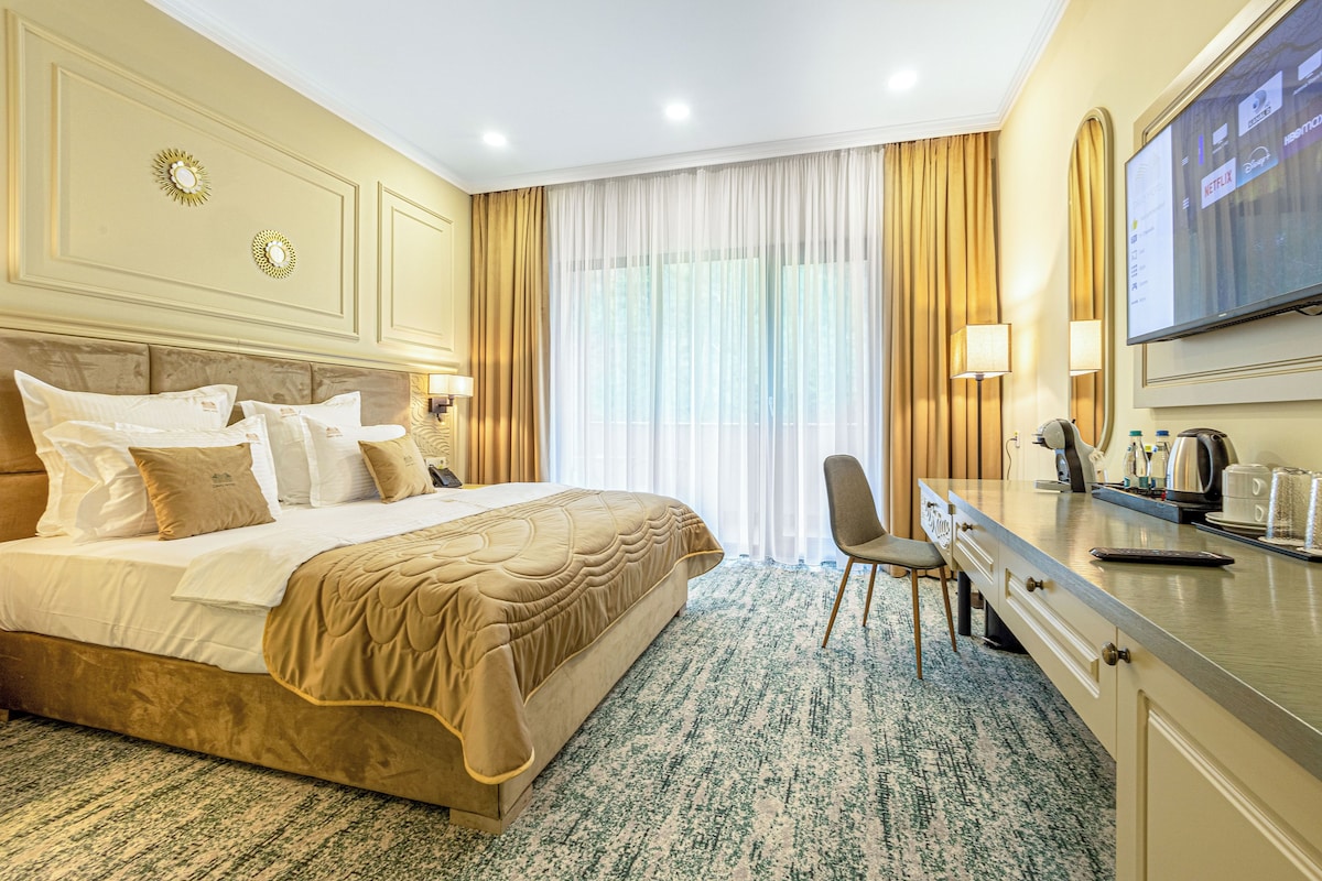 A hotel room with a large bed, a desk with a chair, a television, and a window with curtains.