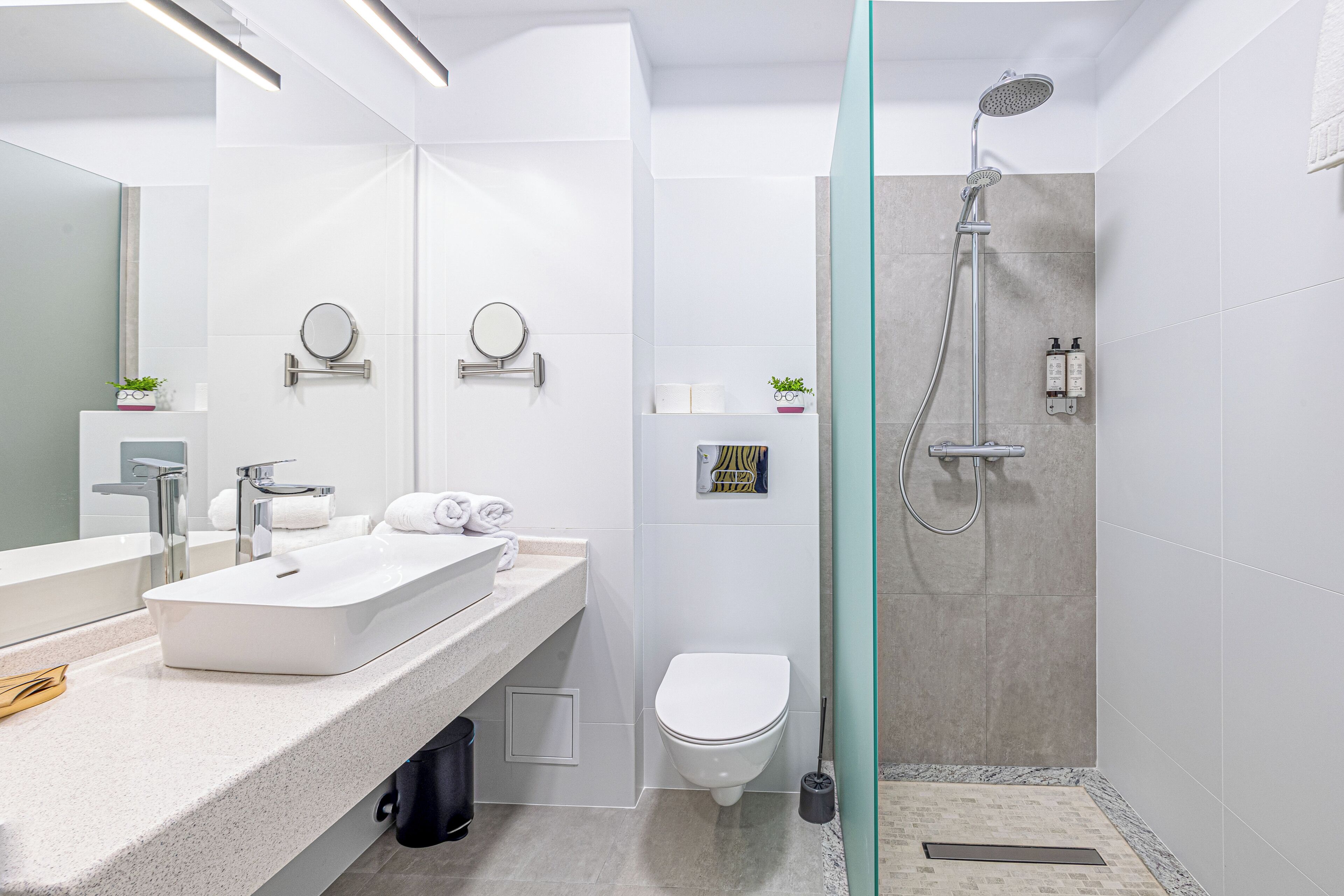 Ein modernes Badezimmer mit großem Spiegel, Waschbecken in Weiß, Toilette und Duschbereich.