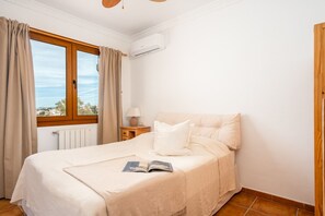 A bedroom with a bed, a window with curtains, a bedside table with a lamp, and an air conditioning unit. - Spacious 4BR Townhouse | Private Rooftop Terrace (Fuengirola)
