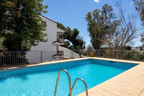 A swimming pool with a metal ladder, surrounded by a fence, and a white building with a balcony in the background. - Spacious 4BR Townhouse | Private Rooftop Terrace (Fuengirola)
