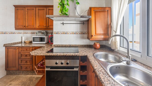 A kitchen with wooden cabinets, a microwave, a stove, and a window with a view. - Holiday Home 'Apartamento Bahía Serena Conil' with Wi-Fi (Conil de la Frontera)