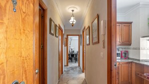 A hallway with wooden doors, framed artwork on the walls, a dining area in the distance, and a kitchen with granite countertops and wooden cabinets. - Holiday Home 'Apartamento Bahía Serena Conil' with Wi-Fi (Conil de la Frontera)